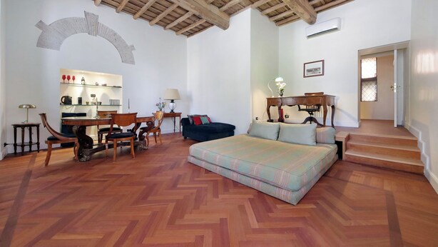 Un'ampia stanza con parquet a spina di pesce, un divano, un tavolo da pranzo con sedie e un angolo cottura sullo sfondo.