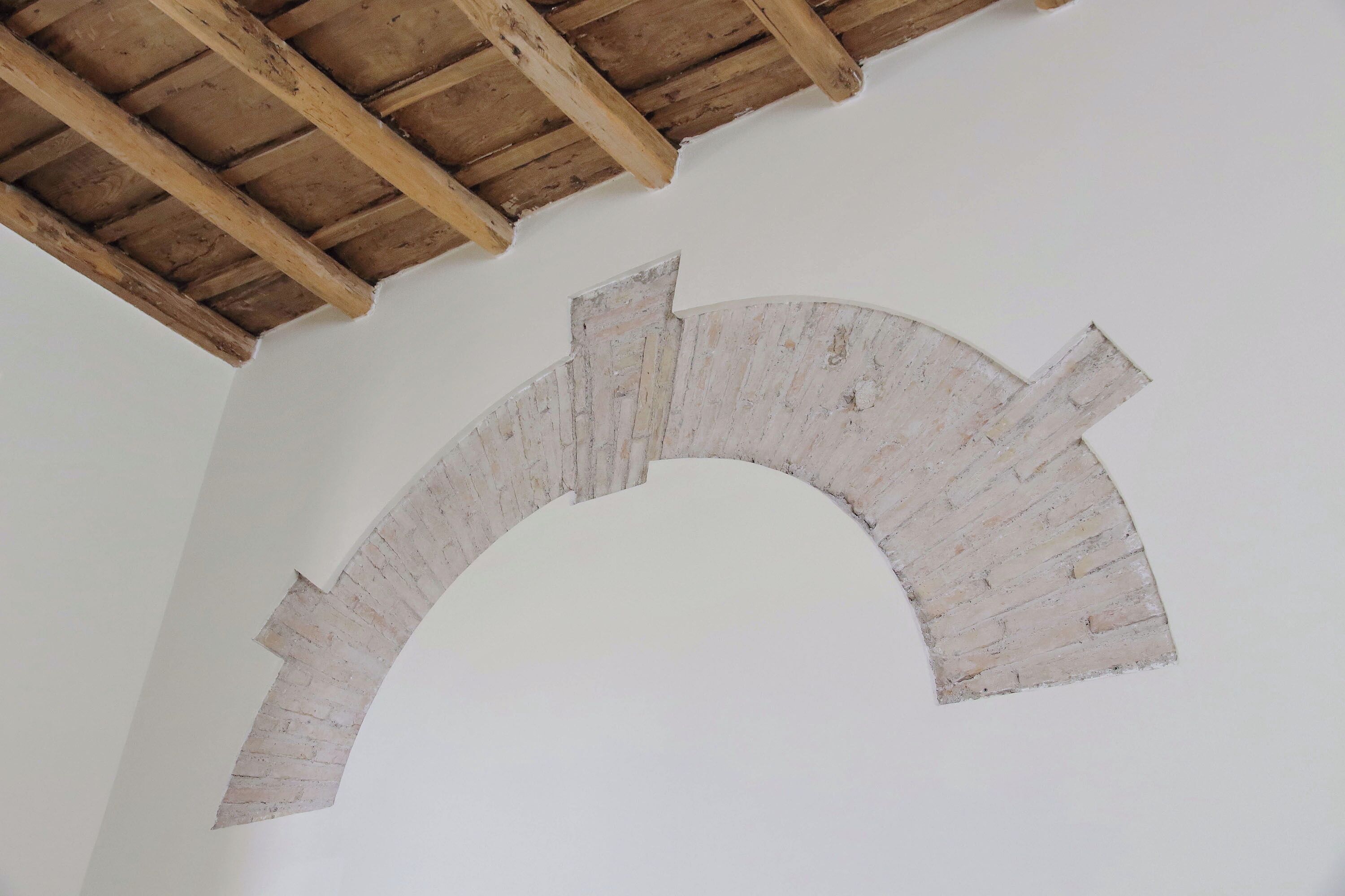 Eine gewölbte weiße Wand mit Holzbalkendecke.