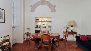 Zona pranzo con un tavolo rotondo, sedie, un piccolo tavolino con una lampada e un divano.