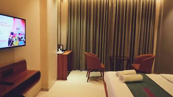 A hotel room with a bed, two chairs, a desk, a TV, and a curtain.