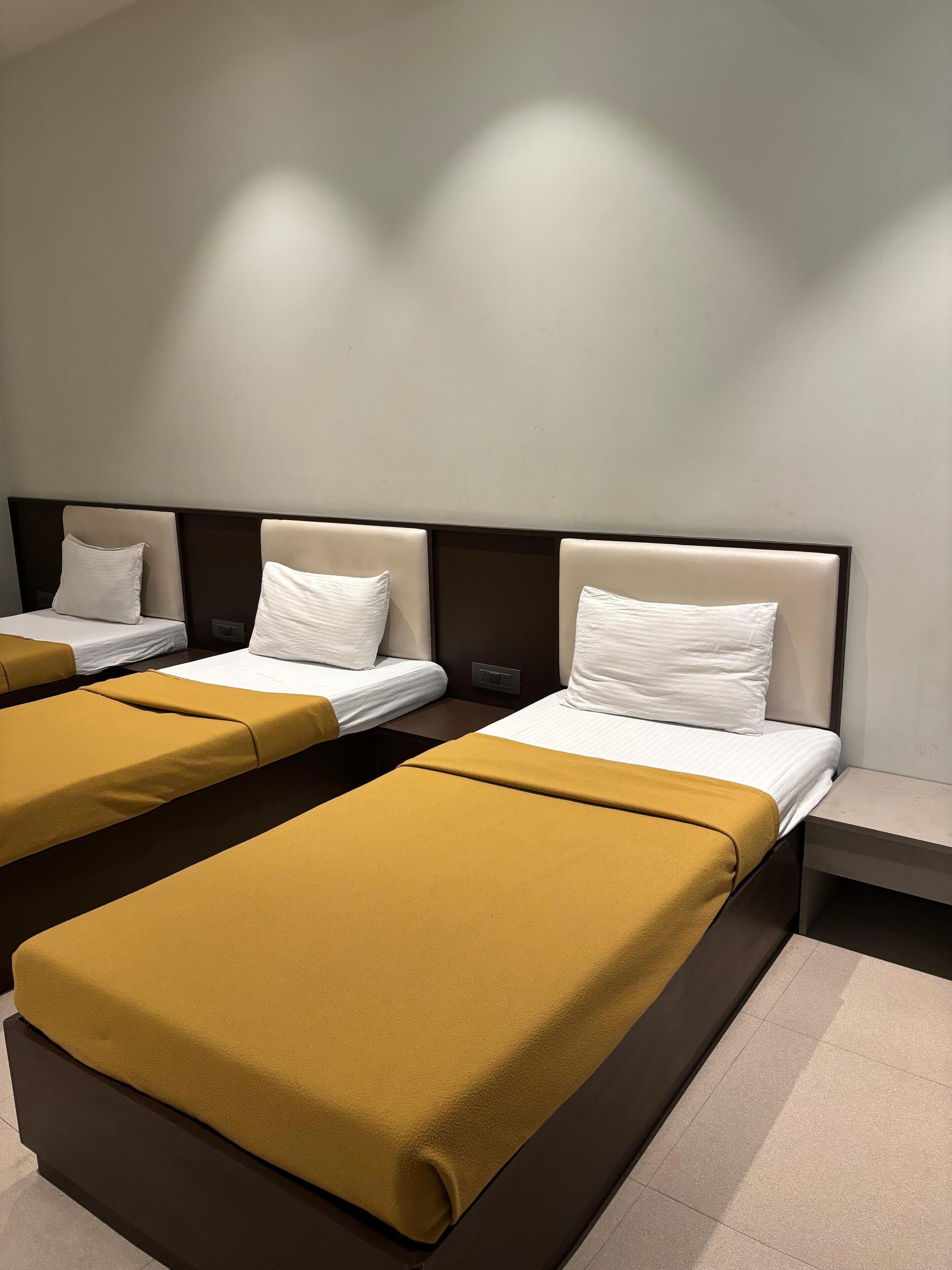 Ein Hotelzimmer mit drei Betten, jedes mit Kopfteil und Nachttisch.