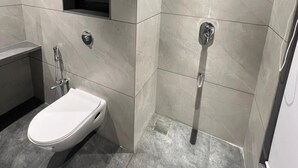 A modern bathroom with a white sink, a handheld showerhead, and a wall-mounted mirror. - Vishram Executive Rooms (Vasai)