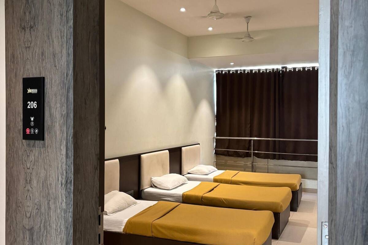 A hotel room with three beds, a control panel, and a ceiling fan.