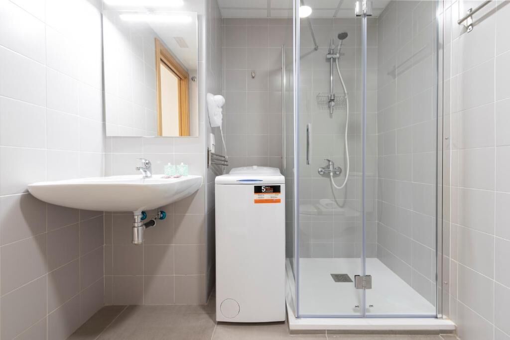 A modern bathroom with a white sink, a glass shower enclosure, and a compact electric heater.
