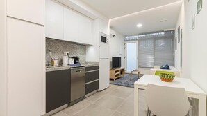 Eine kompakte Küche mit modernen Geräten, ein Essbereich mit einem kleinen Tisch und Stühlen sowie ein Fernseher auf einem Holzboden.