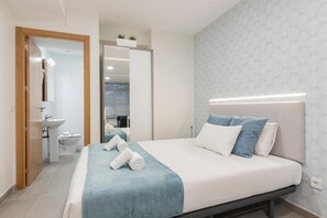 Ein modernes Hotelzimmer mit Bett, Nachttisch, Fenster und einem durchgehenden Türspalt sichtbaren Badezimmer.