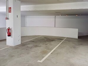 Eine Parkgarage mit weißen Wänden, einem an einer Säule befestigten Feuerlöscher und einer weißen Linie auf dem Boden.