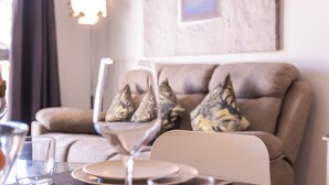 Uma área de refeições com uma mesa posta para dois, um sofá com almofadas decorativas e uma obra de arte emoldurada na parede.