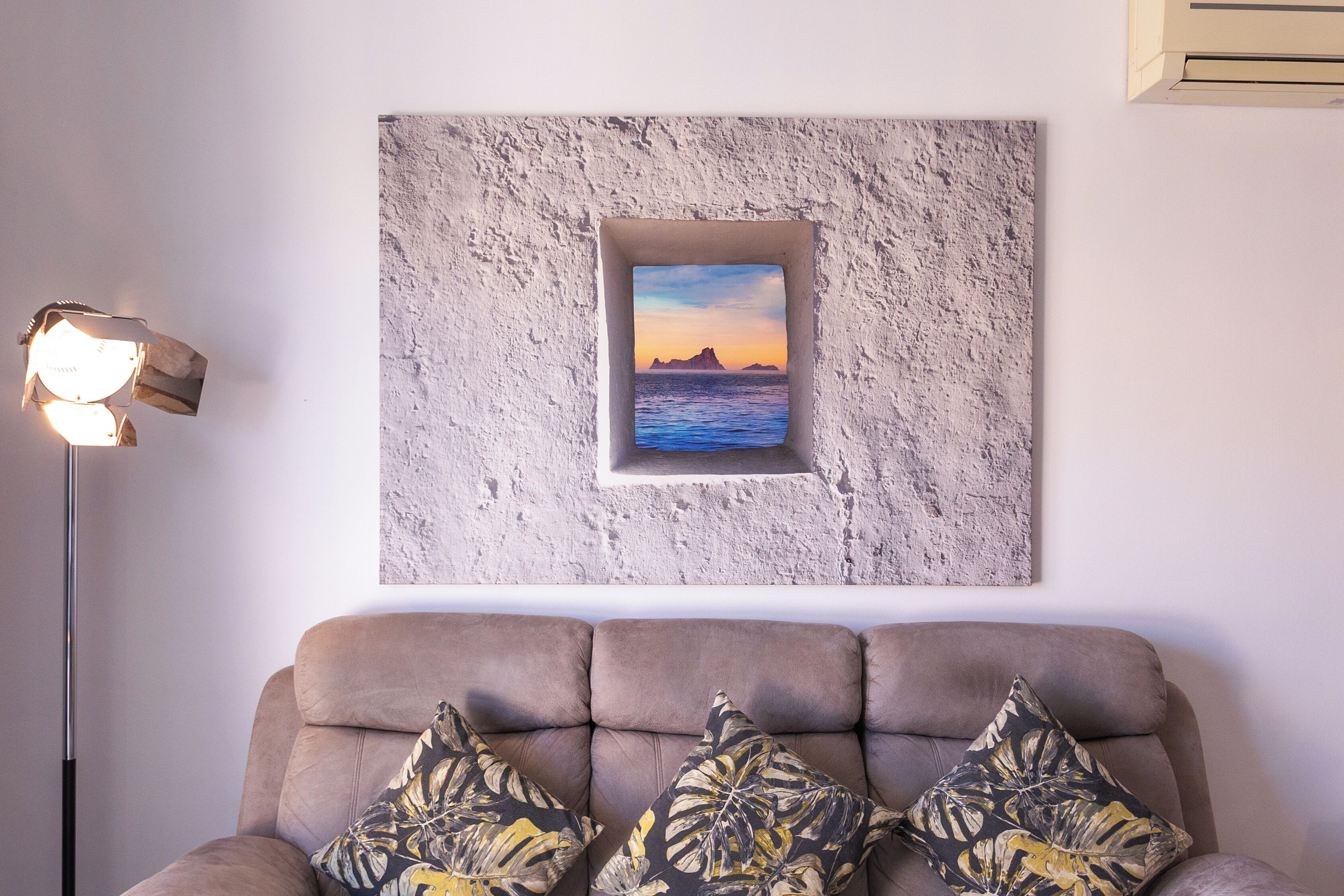 Ein Wohnzimmer mit einer Couch, einem gerahmten Bild von einem Sonnenuntergang über Wasser und einer Stehlampe.