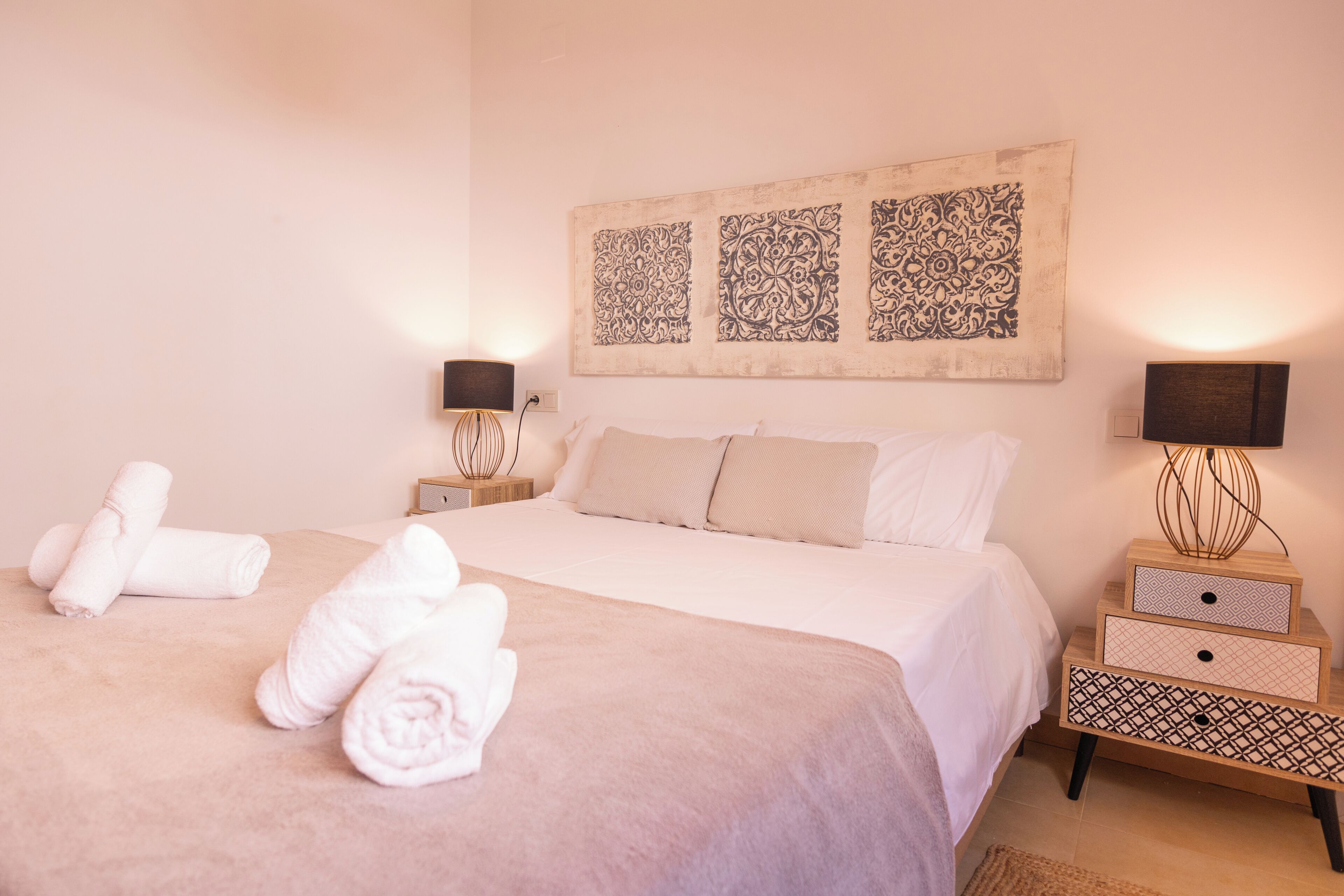 A neatly made bed with white linens, a bedside table with a lamp, and a wall-mounted artwork.