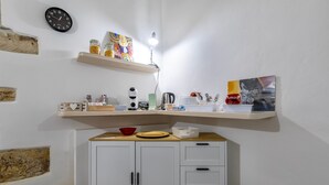 Une cuisine avec des armoires blanches, un plan de travail en bois, une horloge et des étagères remplies de divers objets.