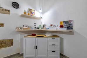 Une cuisine avec des armoires blanches, un plan de travail en bois, une horloge et des étagères remplies de divers objets.
