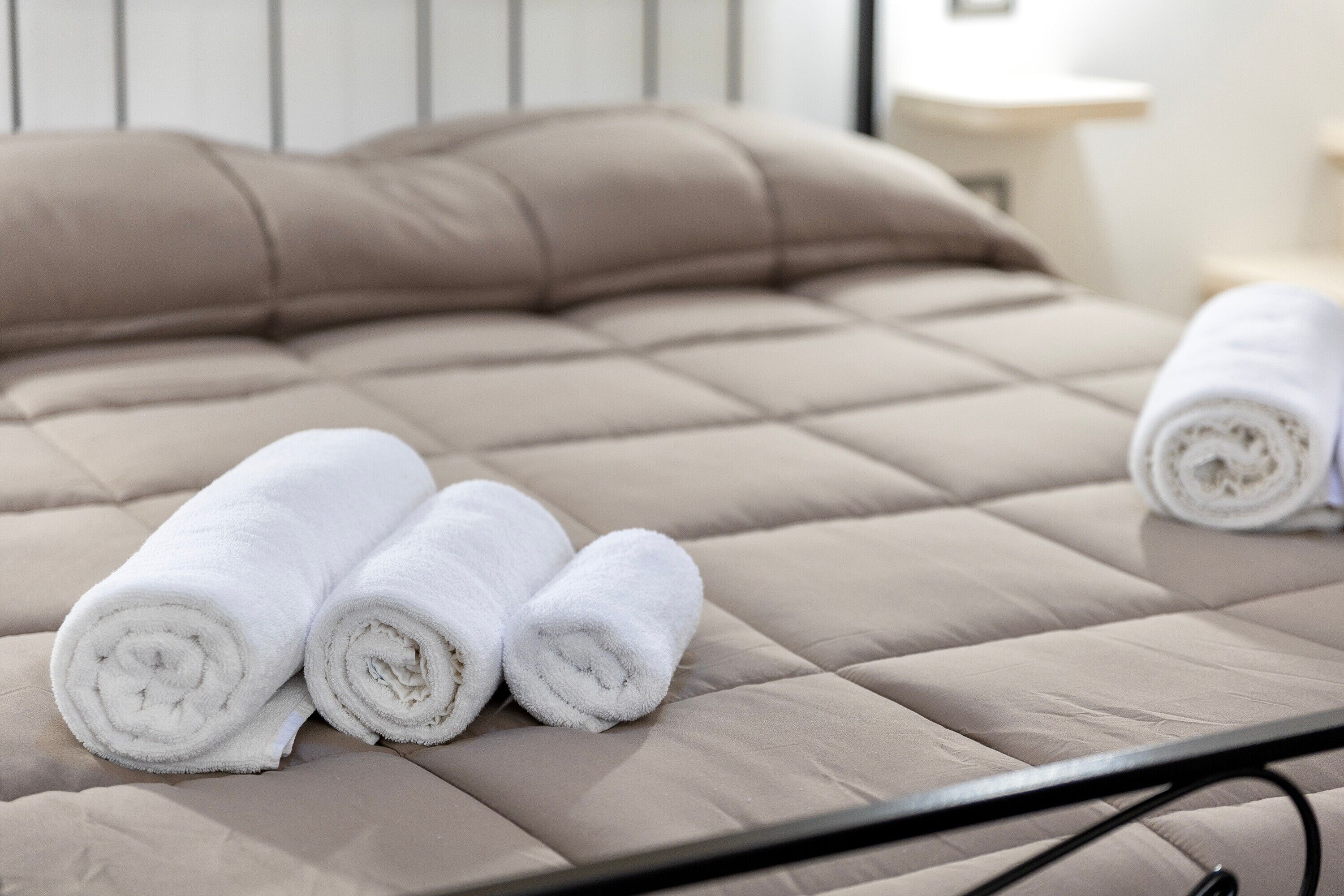A bed with a beige quilted cover and three rolled white towels.