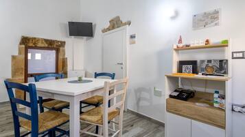 Ein Zimmer mit einem weißen Tisch, blauen Stühlen, einem Holzschrank und einem an der Wand befestigten Fernseher.