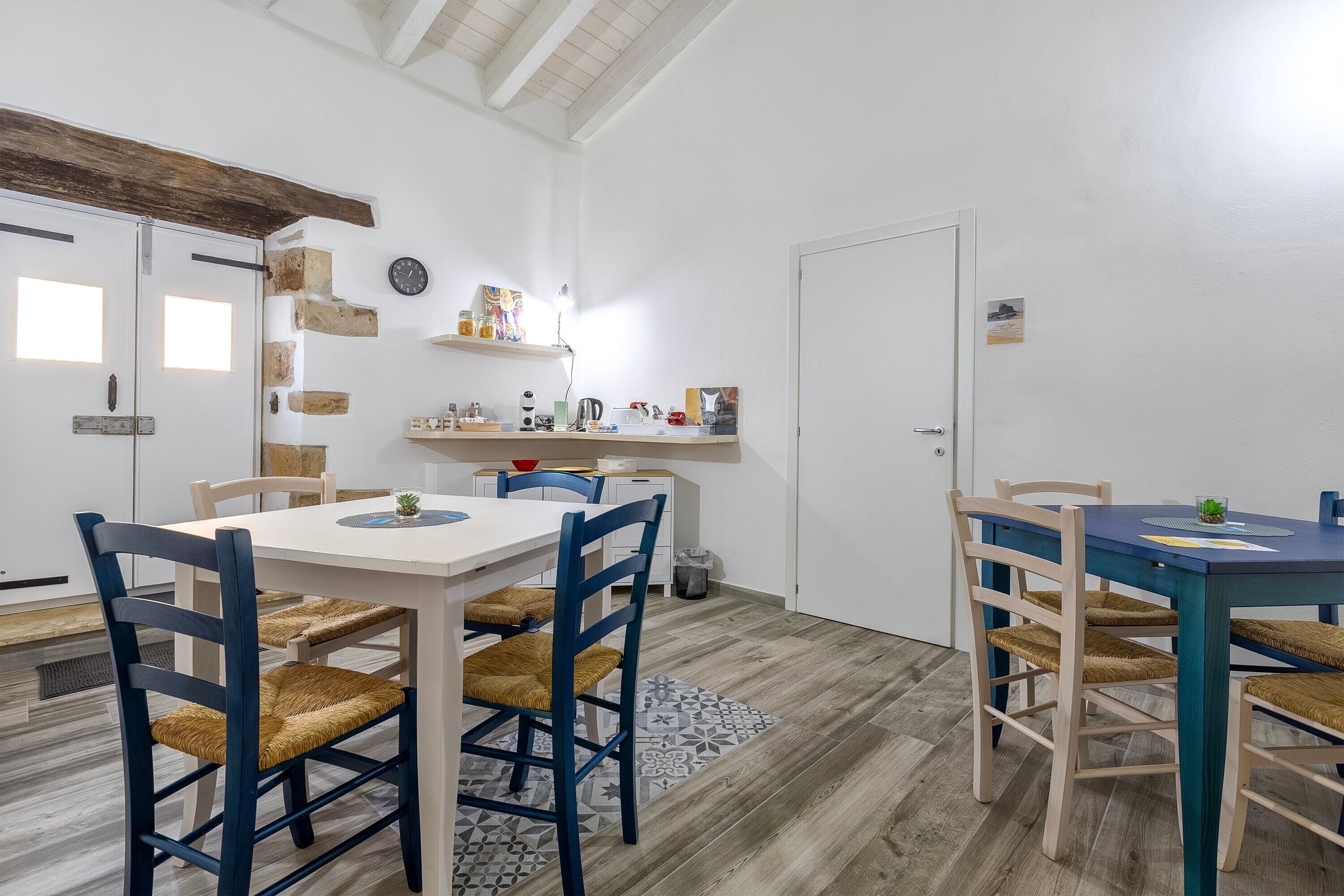 A dining area with two tables, chairs, a clock, and a shelf with various items.