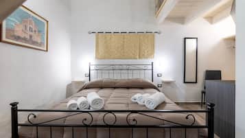Ein ordentlich bezogenes Bett, zusammengerollte Handtücher, ein Bild an der Wand und ein Wandteppich.