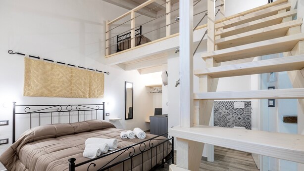 Un dormitorio con cama, espejo, banco y escalera.