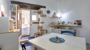 Una cocina compacta con pared de piedra, vigas de madera, una mesa de comedor con sillas y una ventana pequeña.