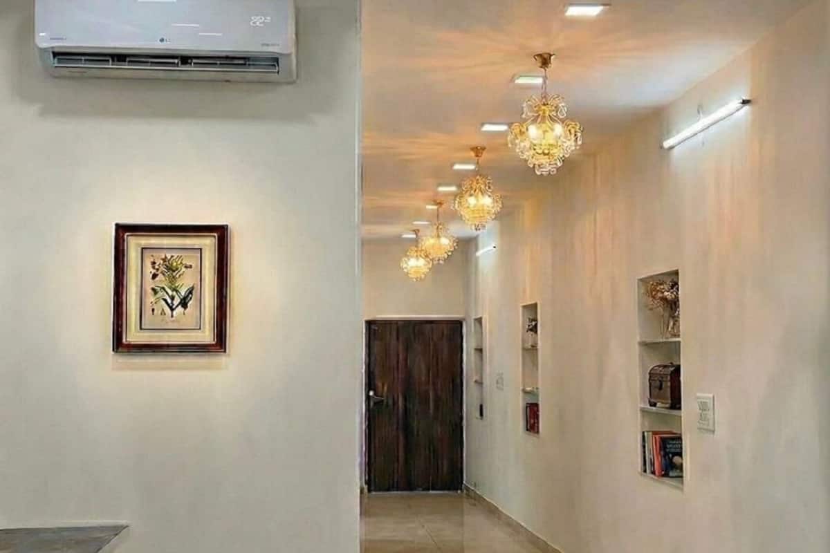 A hallway with a modern air conditioning unit, a framed botanical illustration, and a series of hanging crystal chandeliers.