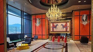 En entréhall med en kristallkrona, inredning i rött och guld, ett stort fönster och utsikt över staden.