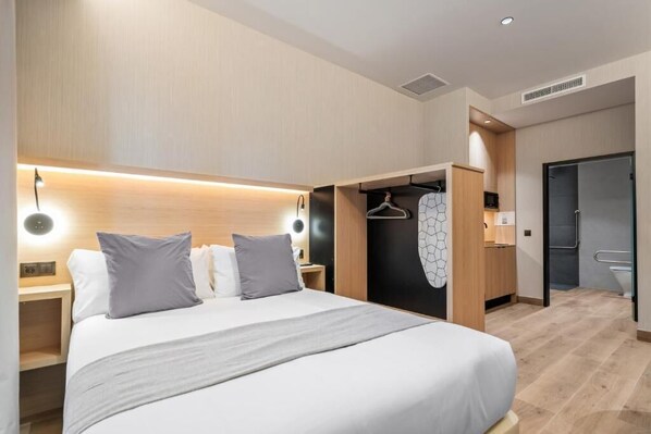 A modern hotel room with a large bed, bedside tables, a built-in wardrobe, and a small kitchenette. - Dobo Madrid Ricardos (Madrid)