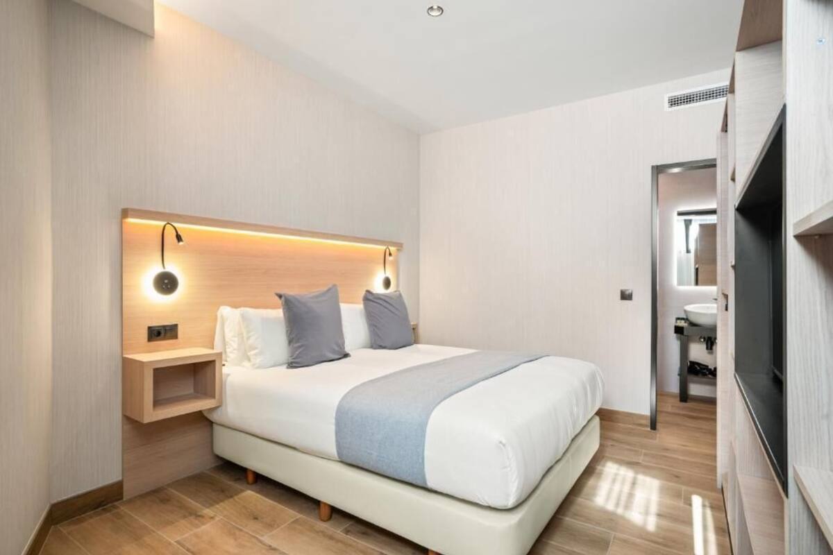 A modern hotel room with a large bed, bedside tables, a built-in TV, and a separate bathroom.