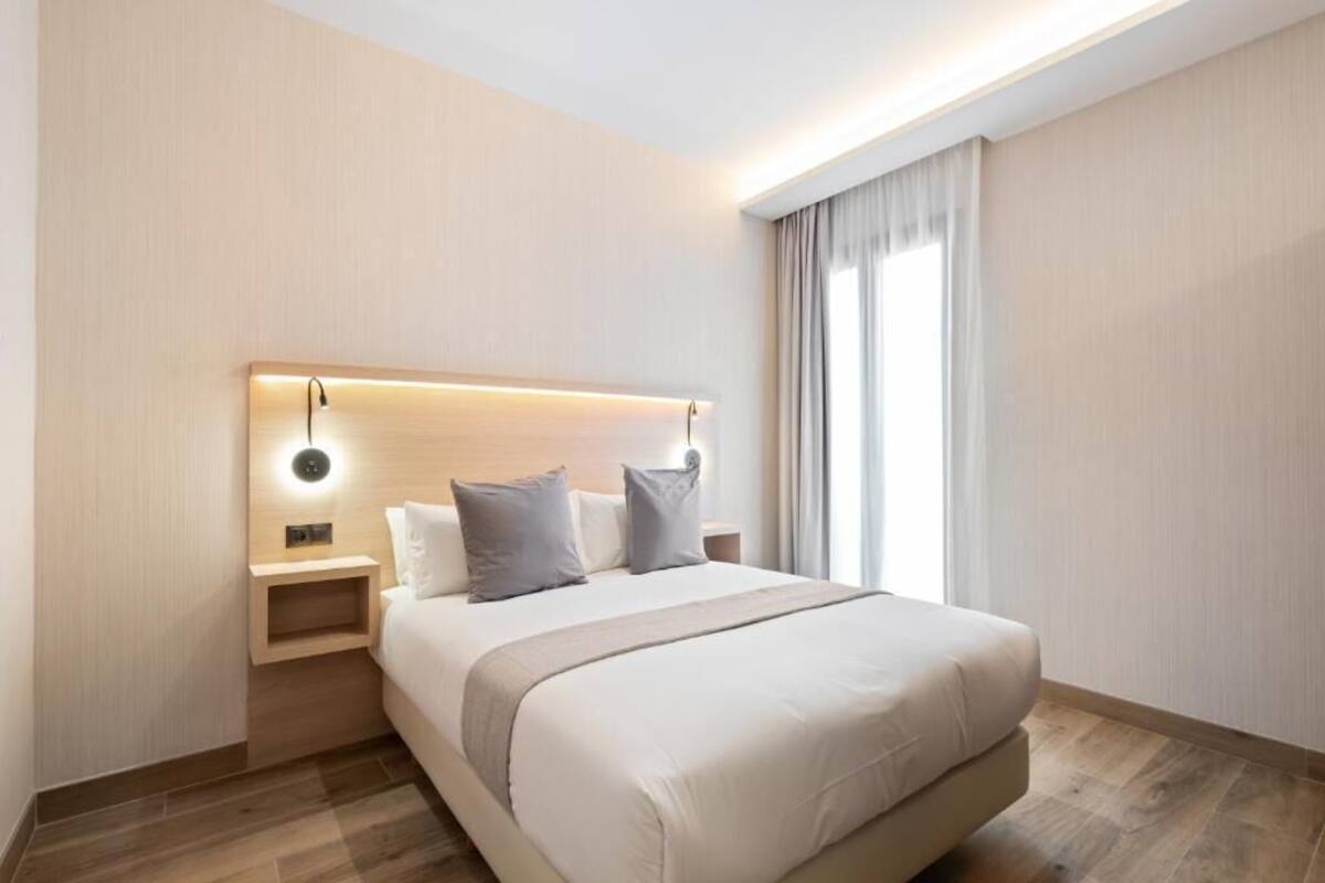A modern hotel room with a large bed, a bedside table, and a wall-mounted light fixture.