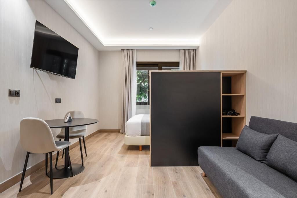 Una habitación de hotel moderna con televisión de pantalla plana, una mesa de comedor con sillas, un sofá y un amplio armario.