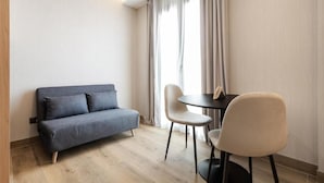 A modern living room with a grey sofa, two chairs, a small round table, and a large window with curtains. - Dobo Madrid Ricardos (Madrid)