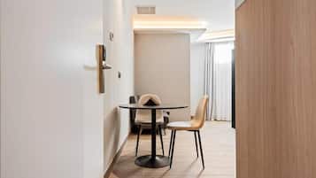 A modern hotel room with a round table and two chairs, a wooden floor, and a view of the outdoors through a window with curtains.