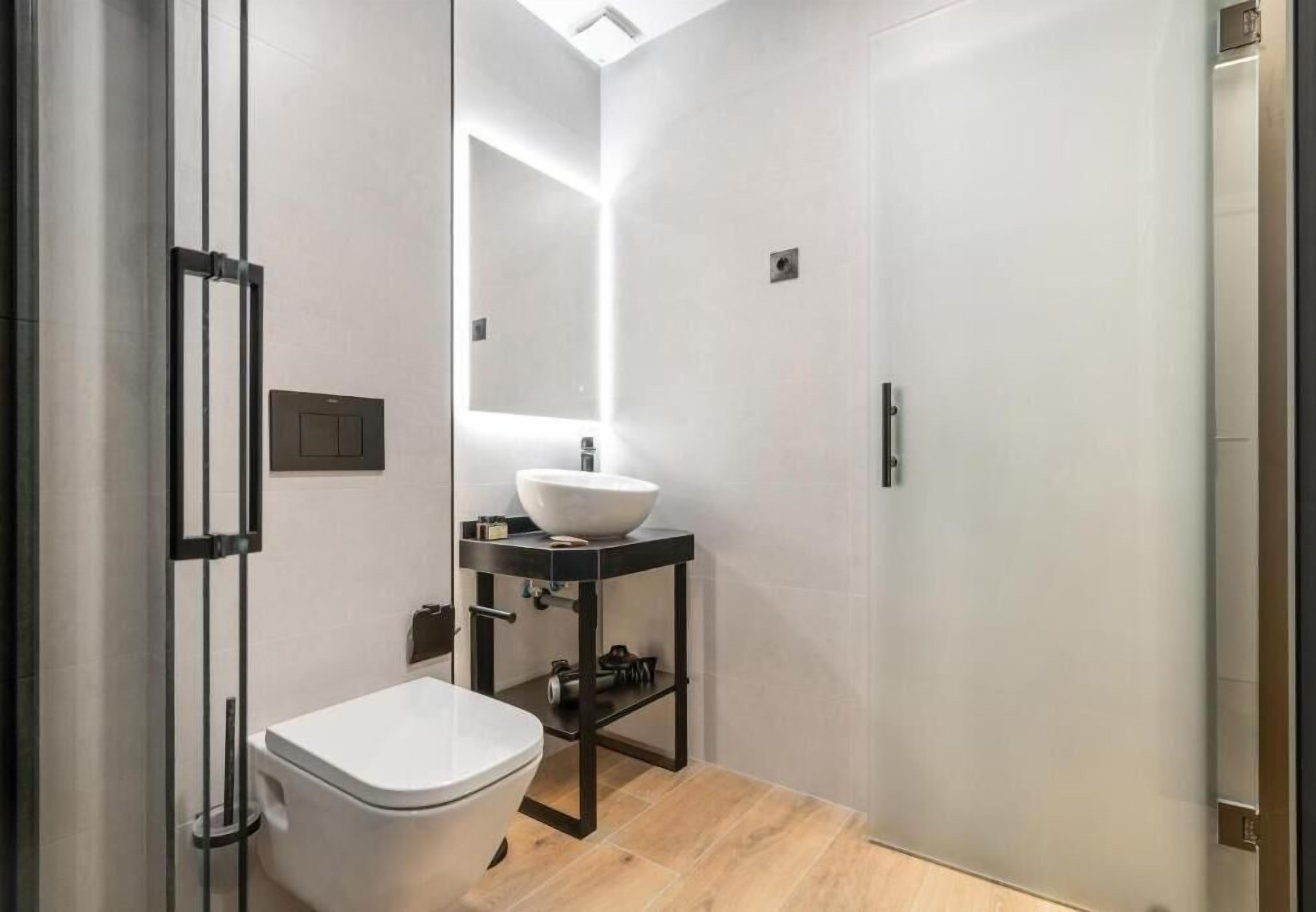 Une salle de bain moderne avec des toilettes blanches, un lavabo sur colonne et un miroir.