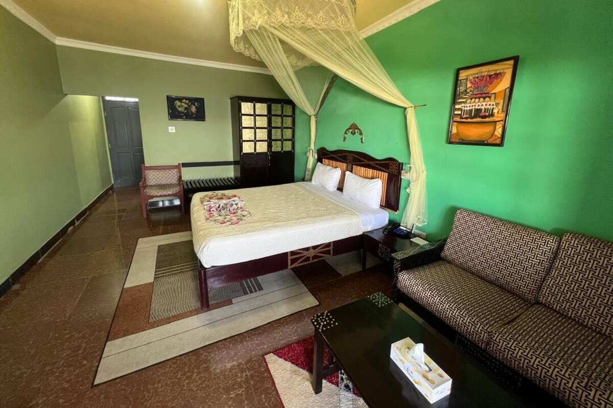 A hotel room with a bed, a sofa, a coffee table, a chair, and a nightstand.