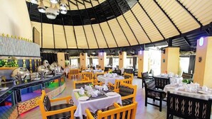 Un restaurant avec des tables rondes et des chaises jaunes, un plafond haut et un coin bar au décor coloré.