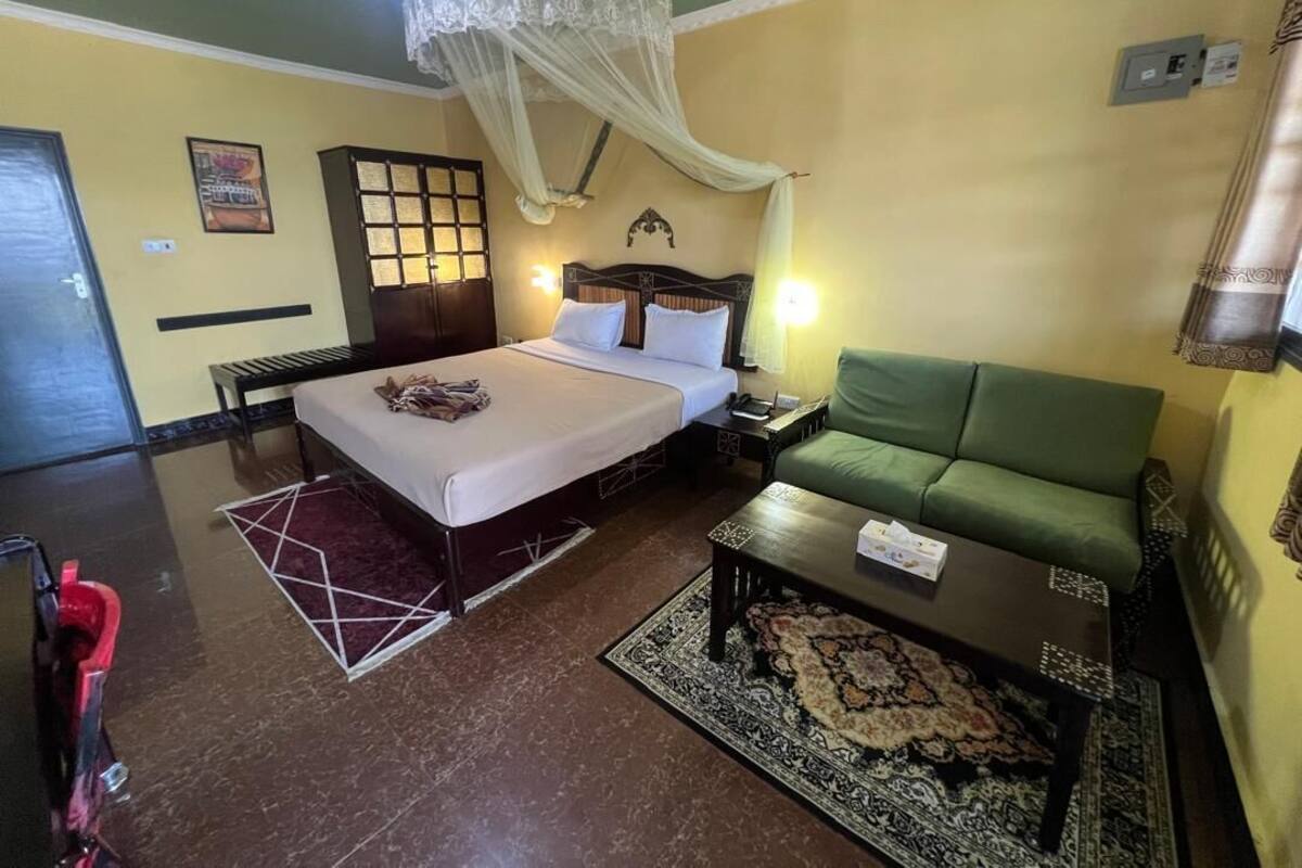 A bedroom with a bed, a green sofa, a nightstand, a lamp, and a decorative canopy.