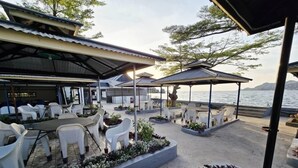 Un espace extérieur aménagé en terrasse, avec des chaises et des tables en plastique blanc, entouré de jardinières contenant diverses plantes et fleurs.