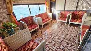 Une pièce chaleureuse, avec des canapés et des fauteuils à rayures, un sol à motifs et une grande fenêtre donnant sur la mer.