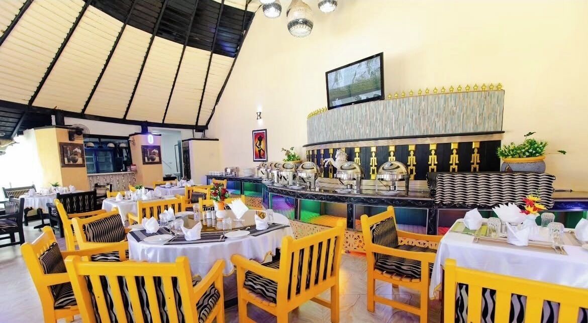 A restaurant with yellow chairs and tables, a counter with food items, and a TV mounted on the wall.