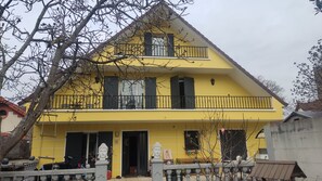 Ein gelbes Haus mit zwei Stockwerken, einem Balkon, einer Statue und einem kleinen Garten.