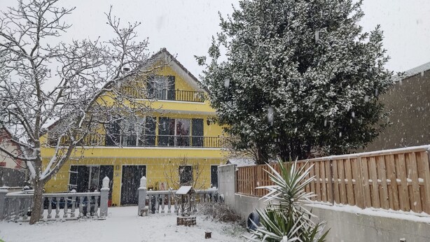 A yellow two-story building with a balcony, surrounded by snow-covered trees and a wooden fence. - Beautiful Chalet-style house. 10 min from Paris (Colombes)