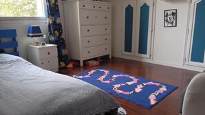A bedroom with a bed, dresser, wardrobe, and a blue rug with geometric patterns. - Beautiful Chalet-style house. 10 min from Paris (Colombes)