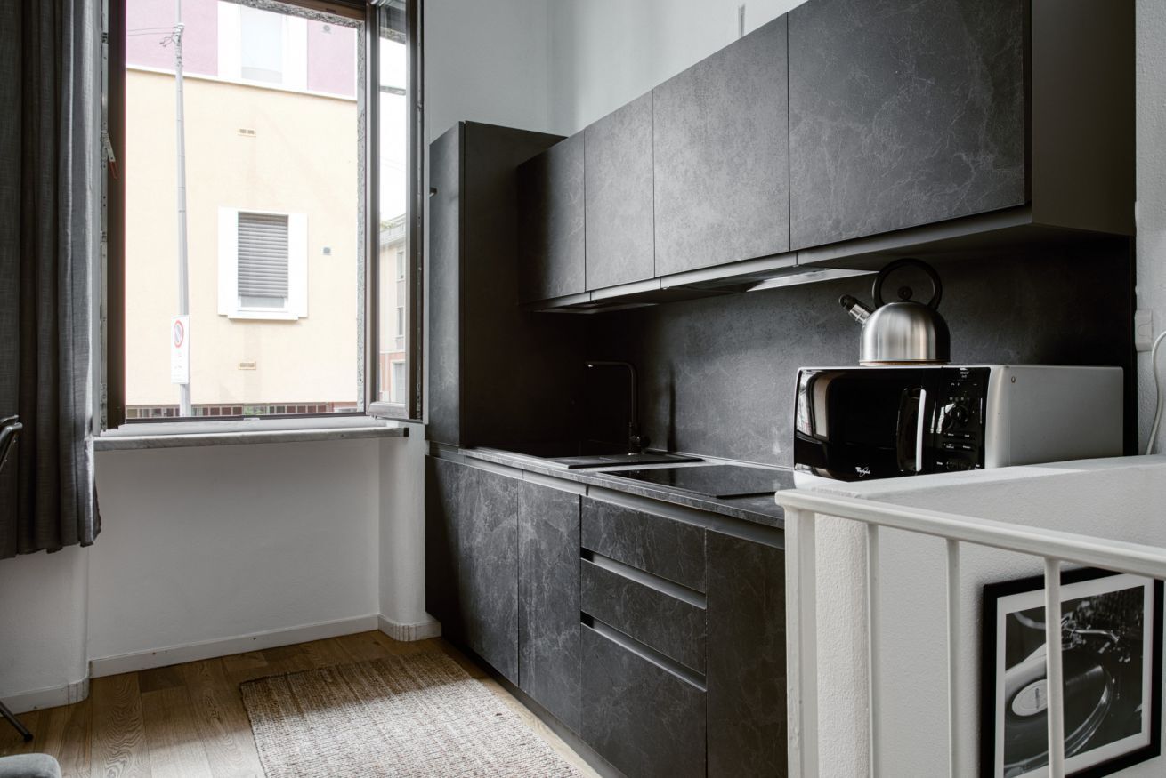 A modern kitchen with dark cabinets, a kettle, and a microwave.