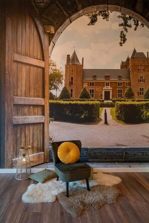 Een kamer met een grote houten deur, een stoel met een geel kussen, een bont tapijt en een muurschildering van een kasteel.