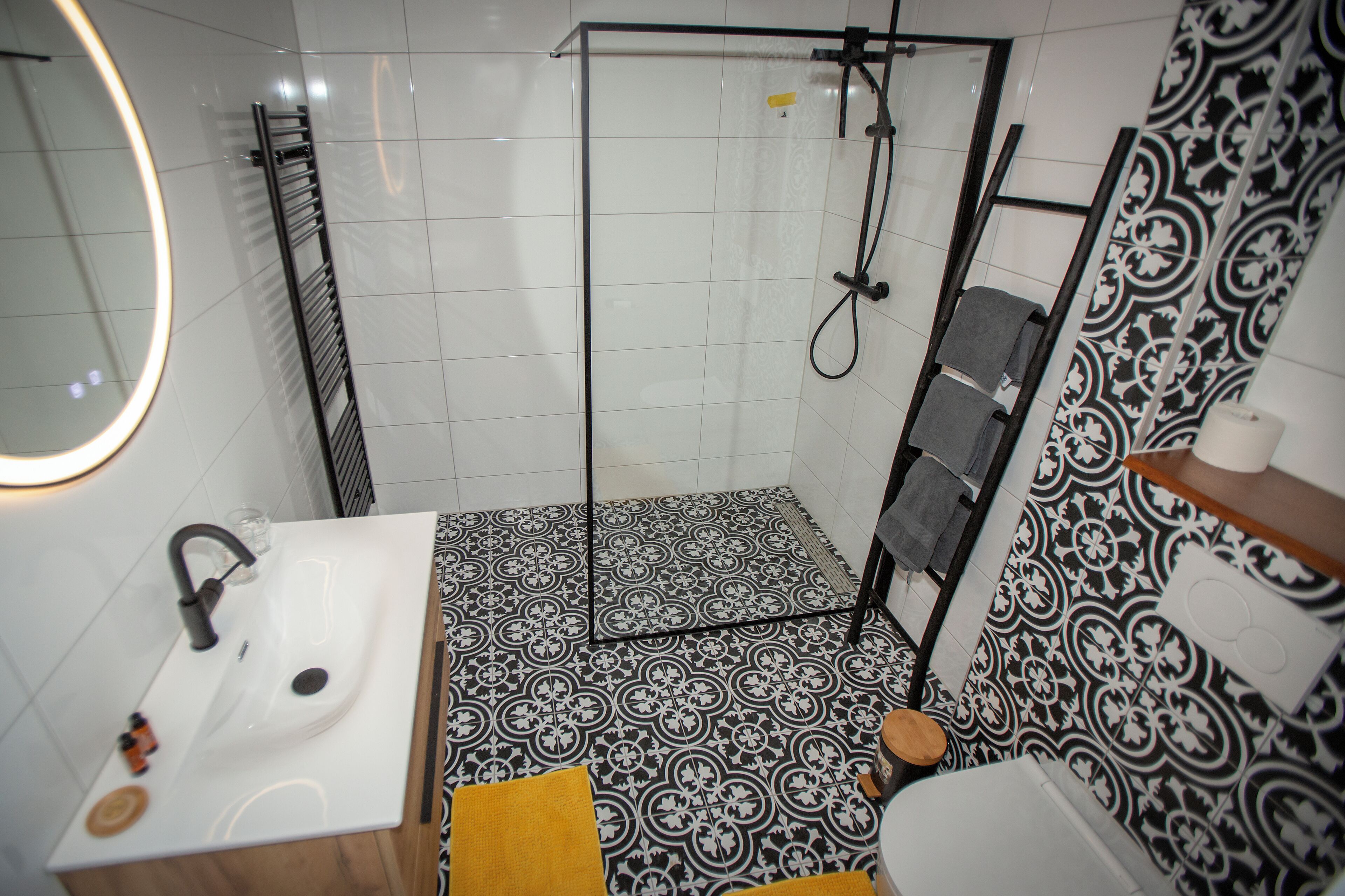 Un baño con ducha, lavabo e inodoro, con azulejos estampados y un espejo.
