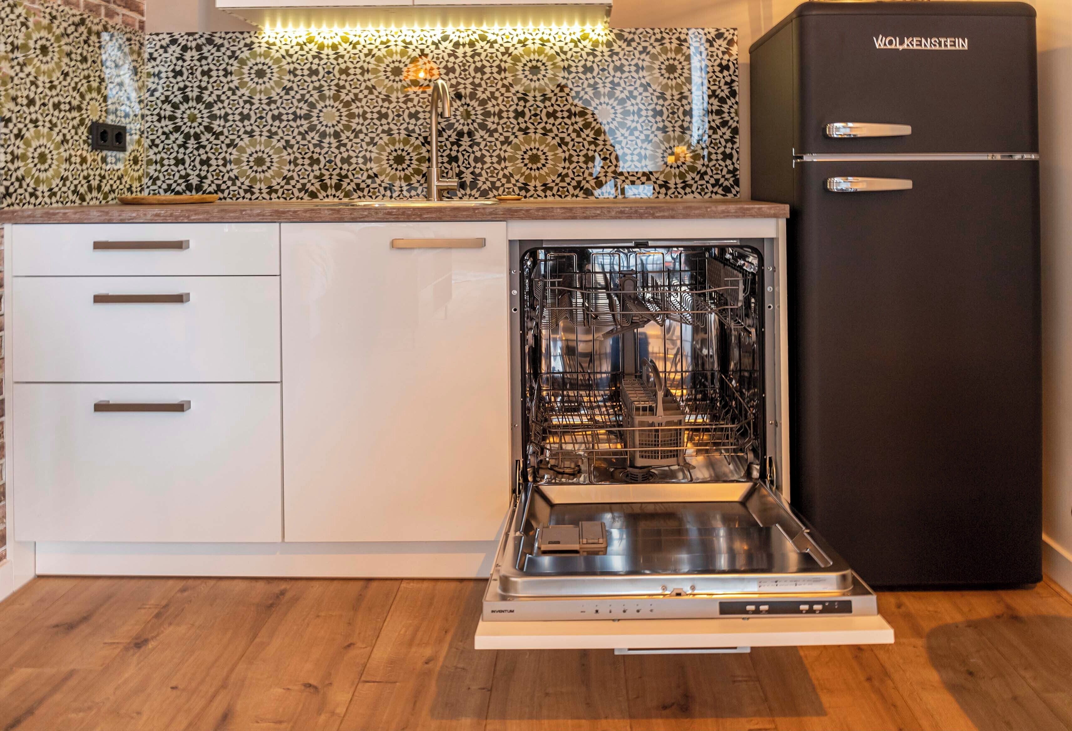A kitchen with a dishwasher, a black refrigerator, and patterned tile backsplash.
