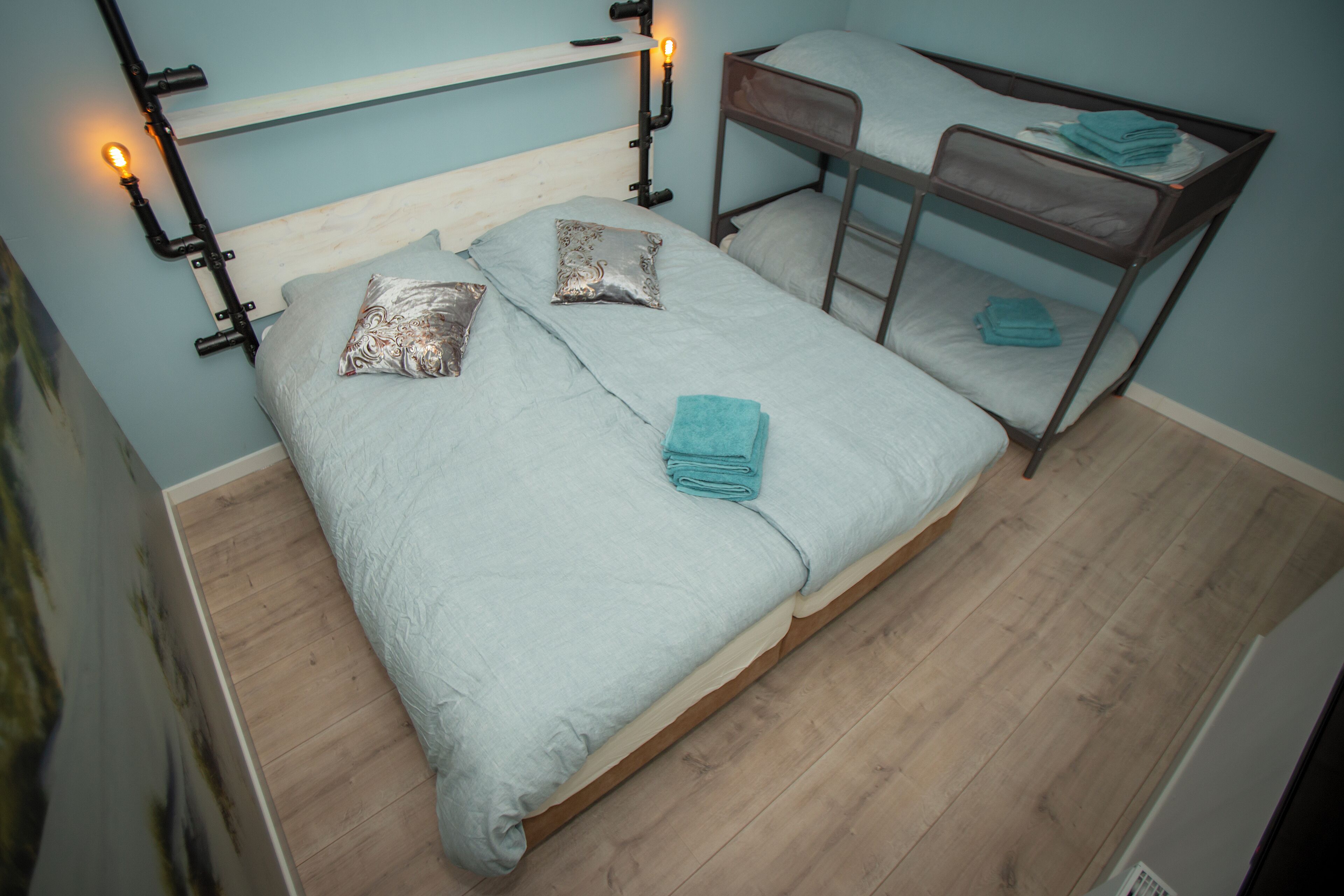 Una cama individual con estructura de madera, dos almohadas, una toalla doblada y una mesita de noche con lámpara.