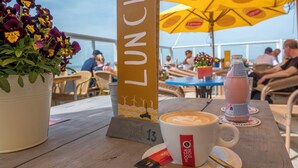 Une table avec une tasse de café, un panneau indiquant « DÉJEUNER » et un parapluie jaune.