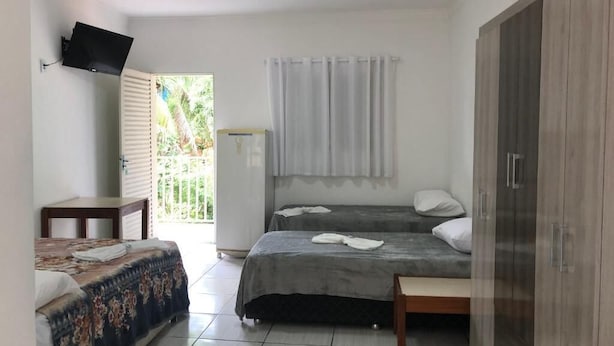 Een slaapkamer met twee bedden, een aan de muur bevestigde televisie, een kledingkast en een raam met gordijnen.