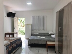 A bedroom with two beds, a TV mounted on the wall, a wardrobe, and a window with curtains. - Hotel alameda  (Várzea Grande)