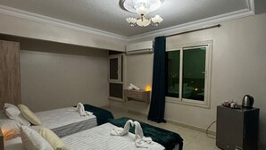 A hotel room with two beds, a ceiling light fixture, an air conditioning unit, and a window with curtains. - Cozy3-bedroom in perfect apartment   view of Pyramids ofGiza Governorate with AC (Giza Governorate)