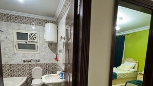 A bathroom with a bathtub, sink, toilet, and a window with a fan. - Cozy3-bedroom in perfect apartment   view of Pyramids ofGiza Governorate with AC (Giza Governorate)